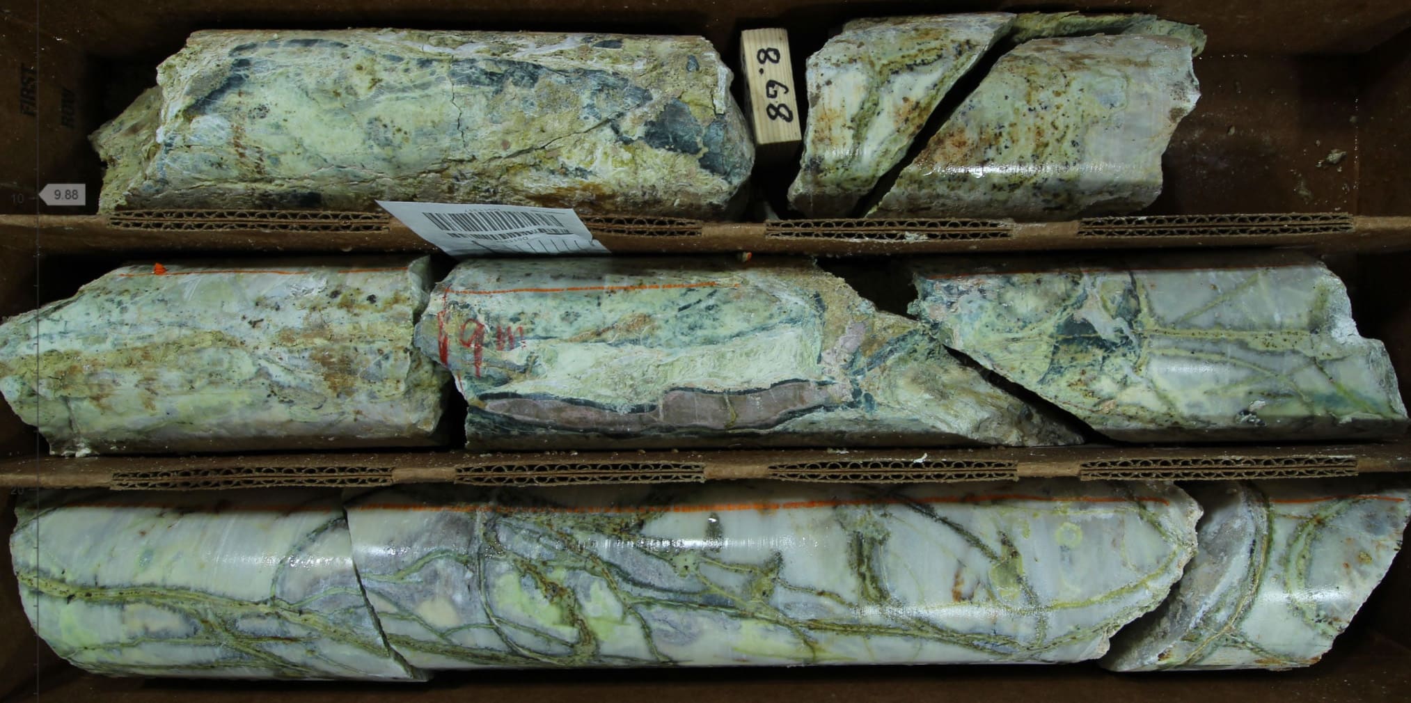 Dark grey limestone recrystallized to marble, with intense stockworks of dark green pyroxene veins cored by quartz and sulfide altering to yellow-green nontronite clay and copper oxide minerals (Hole 002; 9 m; PQ core).